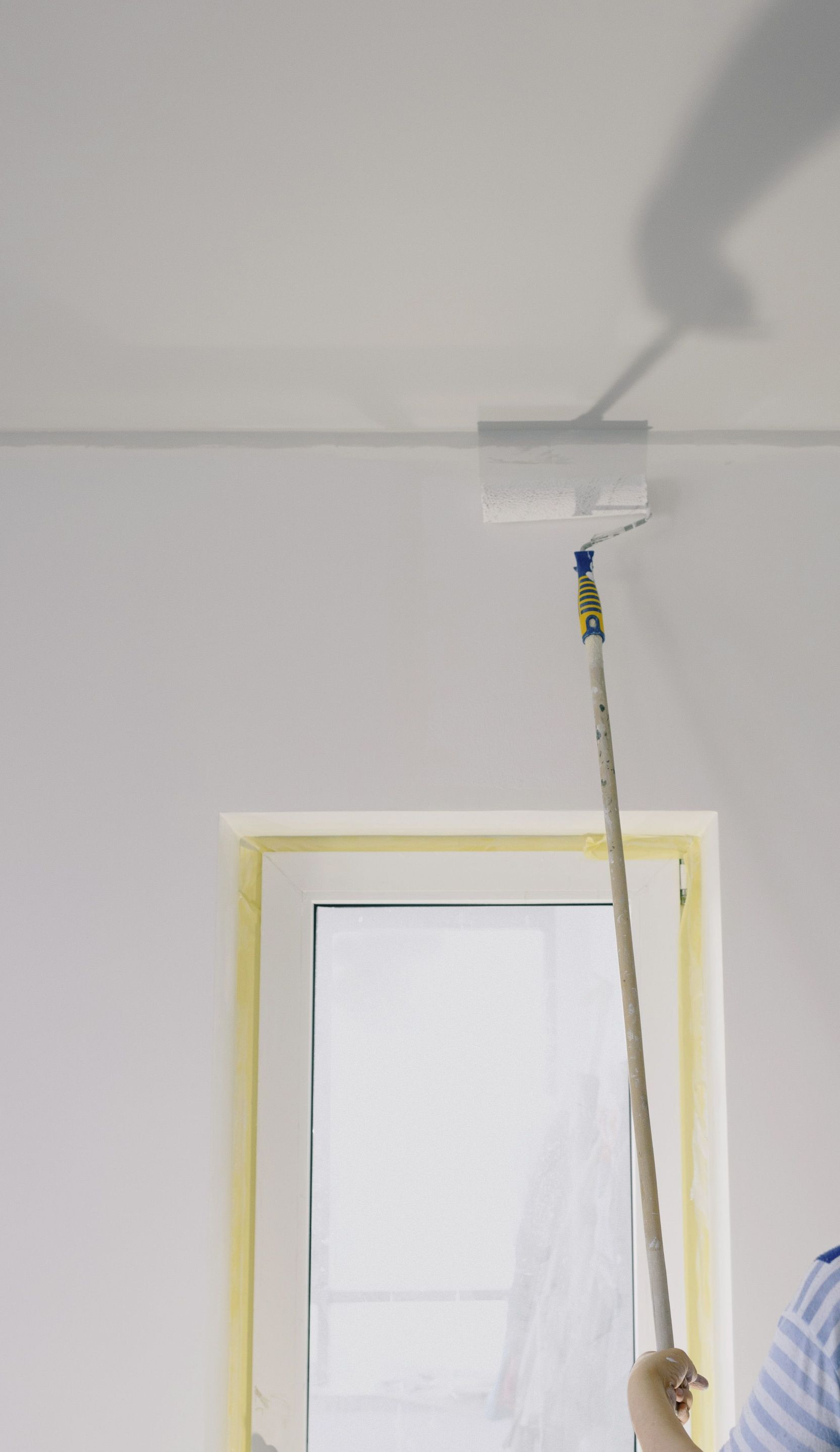 Crop faceless female holding paint roller and renovating walls in room at home